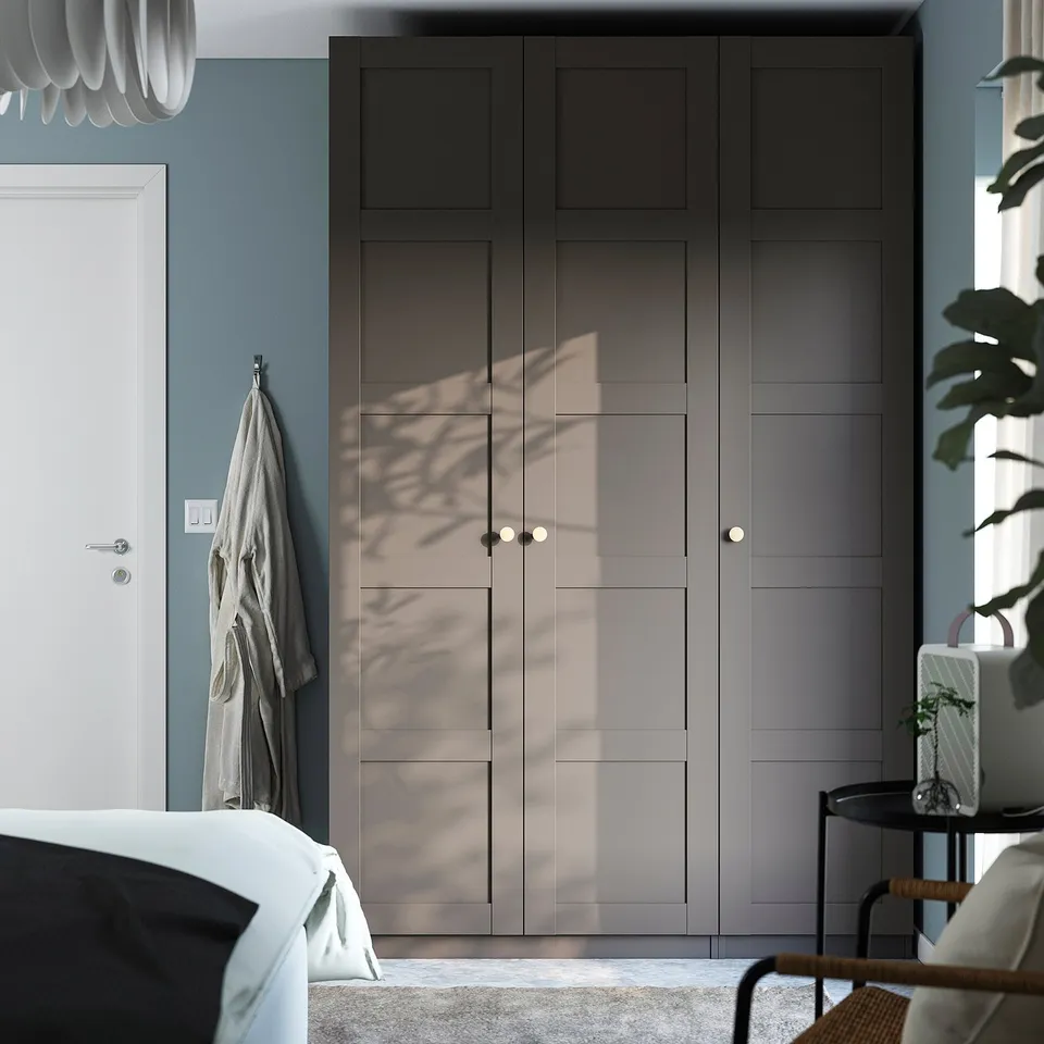 Modern PAX wardrobe, grey, with sunlight patterns, flanked by door and plant.
