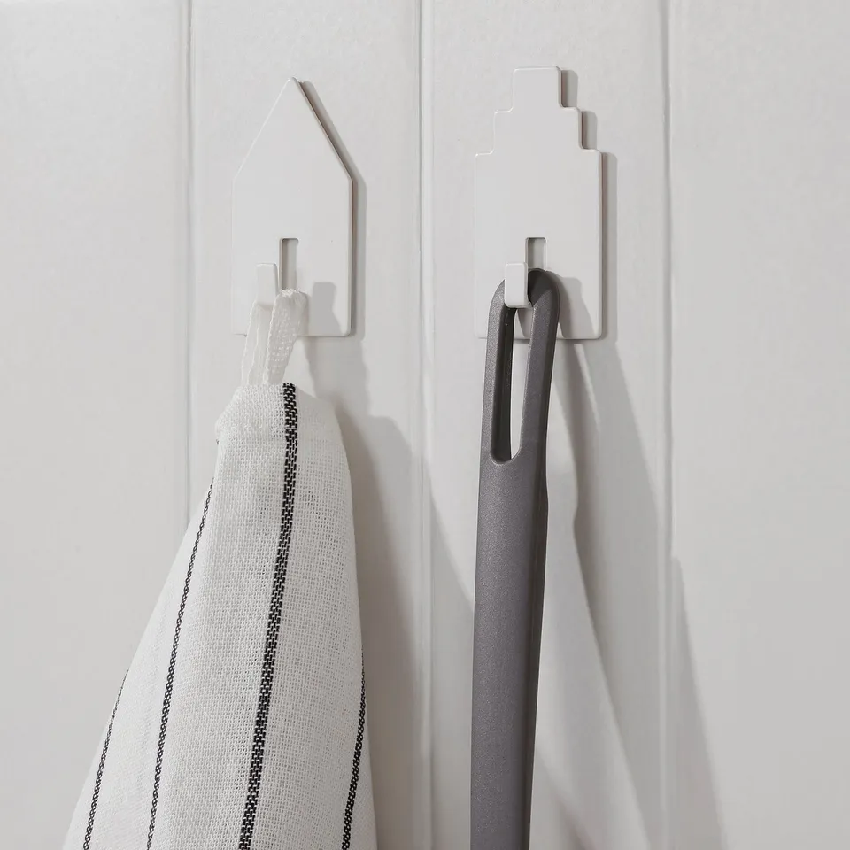 Two modern wall hooks hold a striped cloth and a black item, demonstrating their use for storage and organisation.