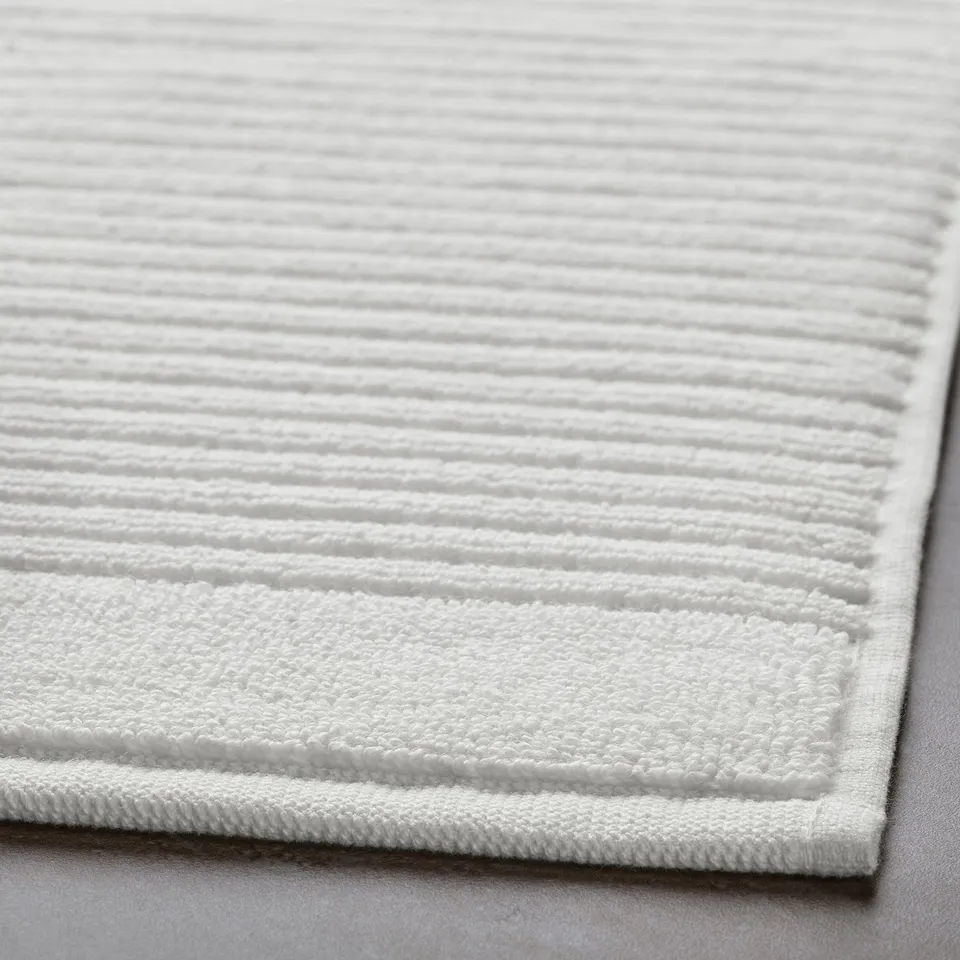 Close-up of a textured, pure cotton bath mat with a white terry weave and bordered edges.