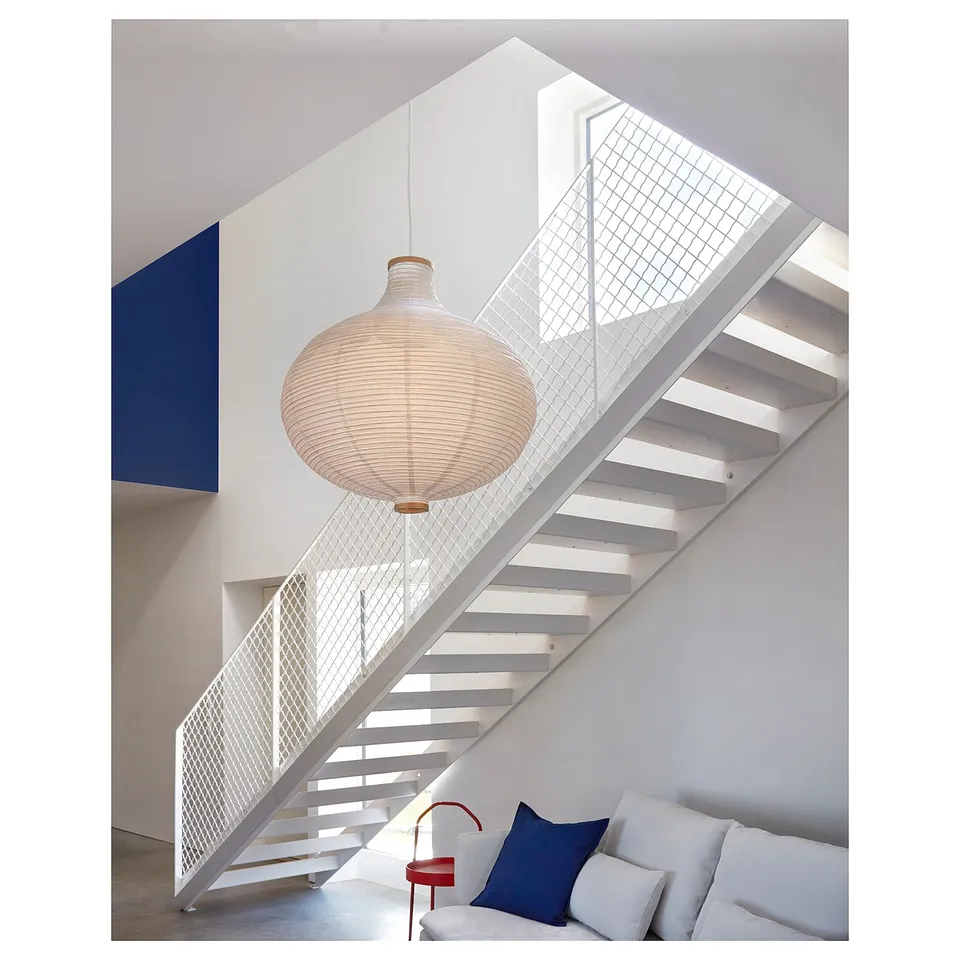 Modern staircase with white steps, metal railing, large woven pendant lamp, and white sofa with blue pillow.