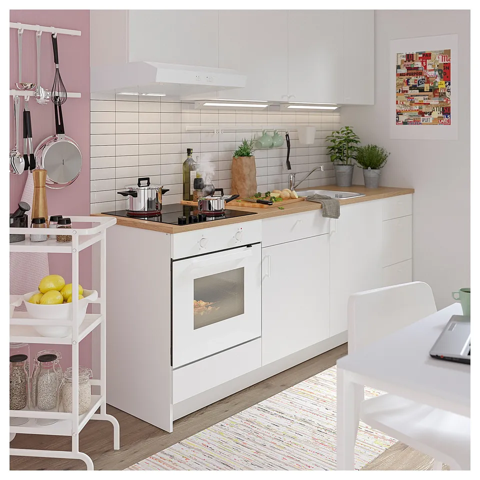 Modern white kitchen with wooden countertops, featuring a built-in hob, oven, and hood. Led lighting, utensils, and plants decorate the space.