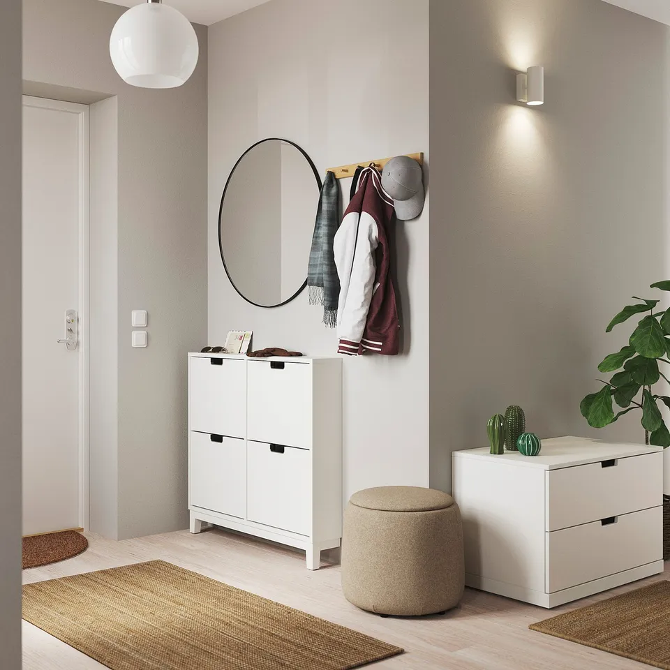 Modern entryway with white furniture: a round mirror, wooden coat hangers, and a white shoe cabinet & stools. Plants and beige rugs enhance the decor.