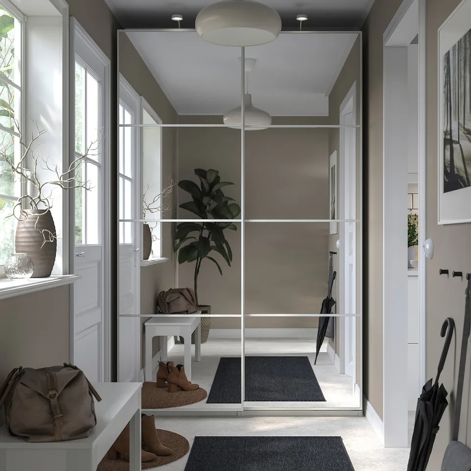 Modern entryway with white PAX wardrobe, glass doors, grey rugs, and potted plant.