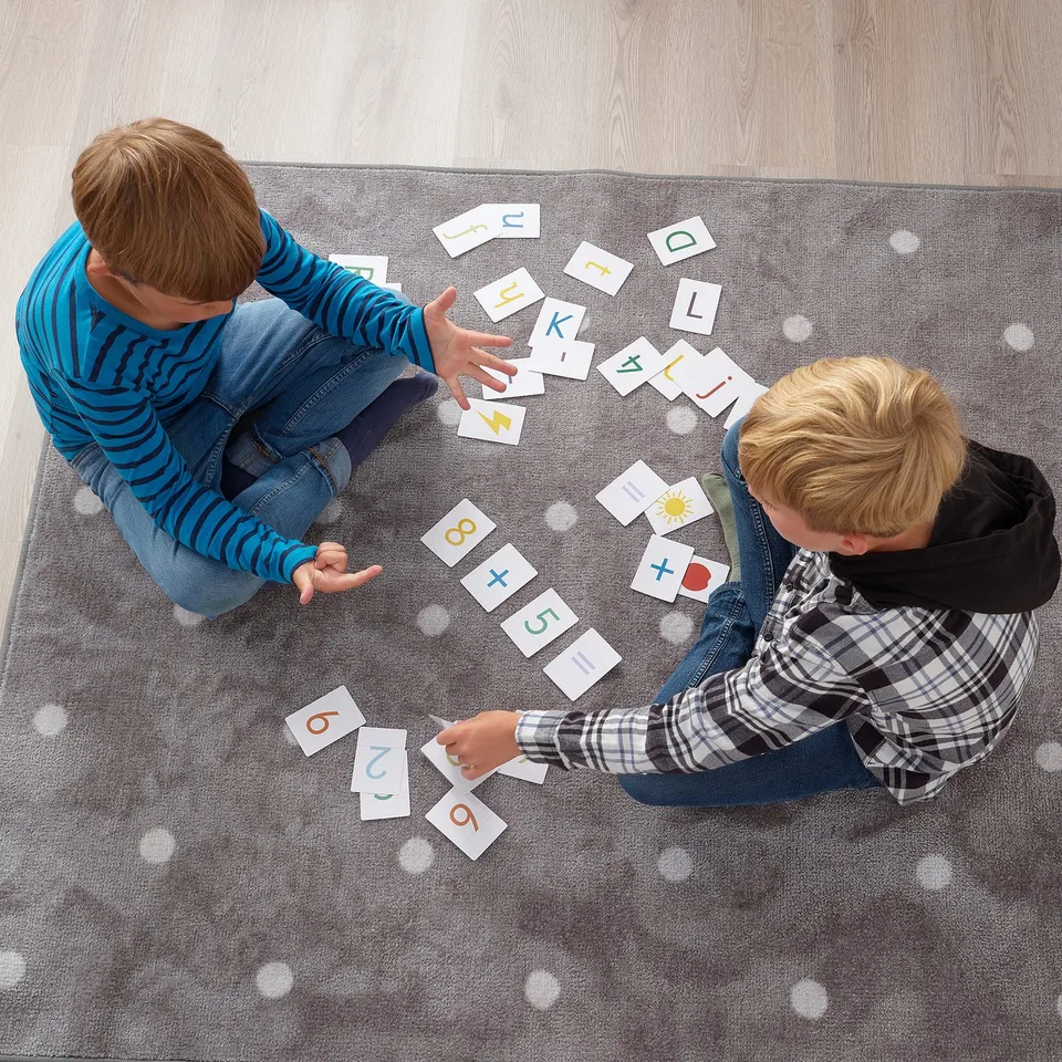 Two children playing with alphabet and number cards, matching and learning letters and numbers on a grey rug.