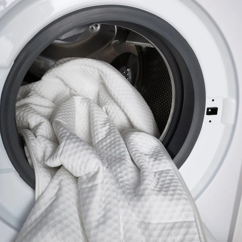 Image shows washing a memory foam mattress cover in a front-loading washer.