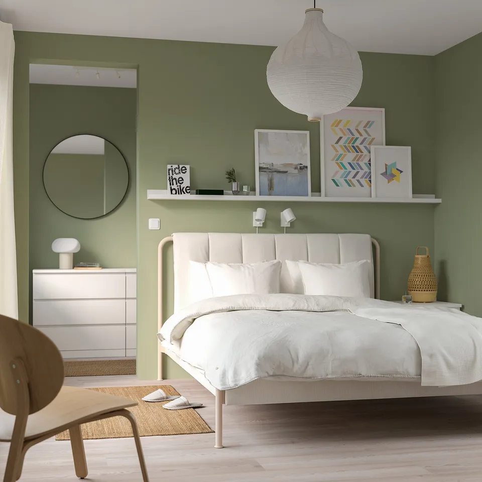 Modern bedroom with TÄLLÅSEN bed, light beige, green walls, mirror, dresser, chair.