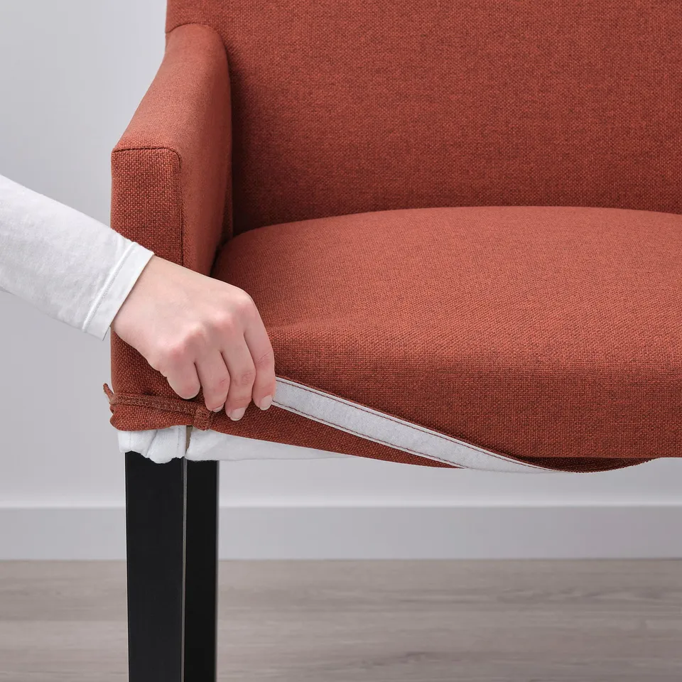 Hand pulling up orange MÖRBYLÅNGA chair seat cover, revealing silver zip.