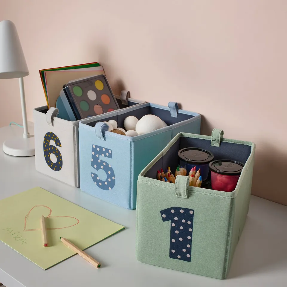 Three labelled fabric storage boxes with items, desk, lamp, note. Kids room decor.