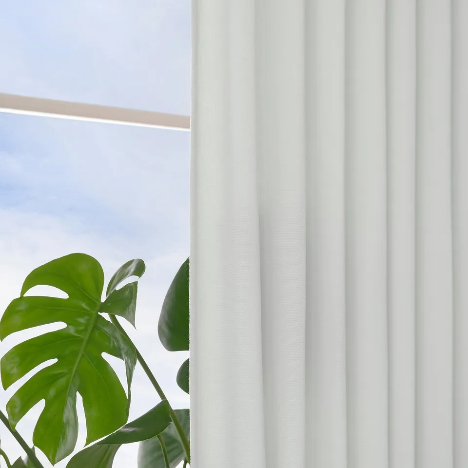 Vertical-striped white curtains allow daylight and privacy, with a green plant below for a serene feel.