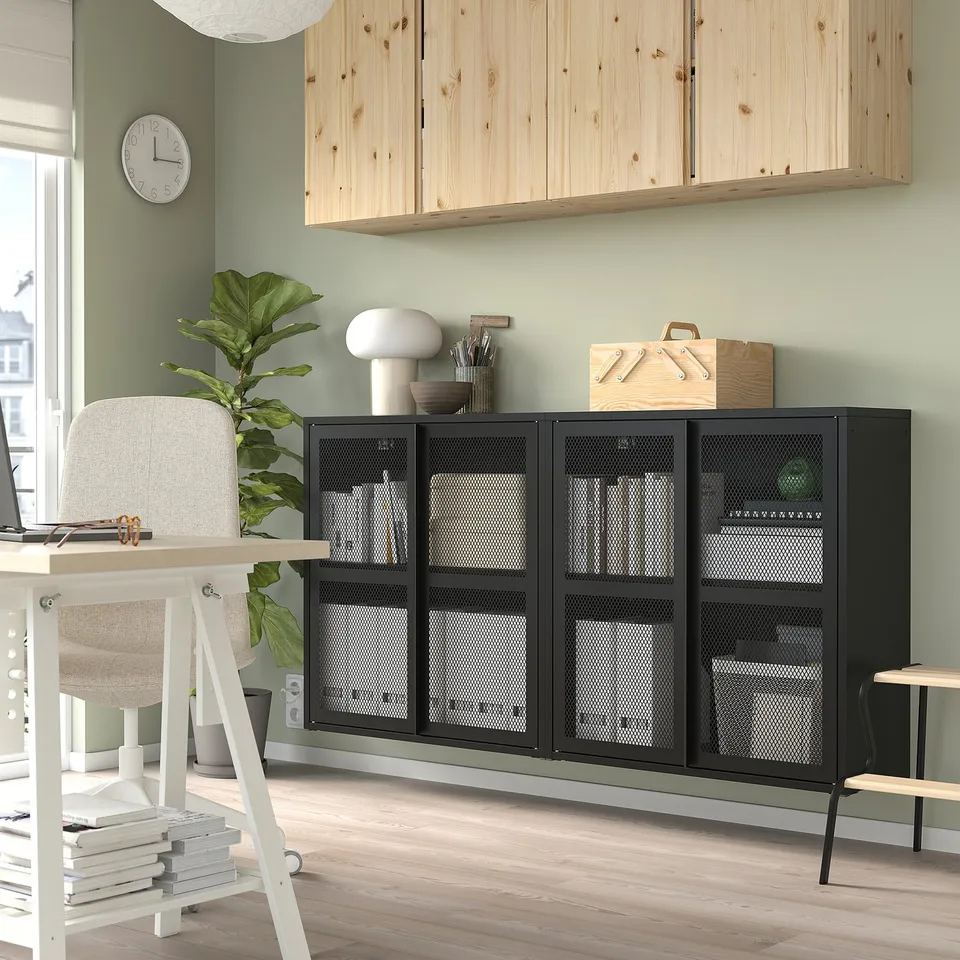 Black IVAR metal storage cabinet with mesh doors; large, sleek, modern design; stands tall near desk, fits various rooms.