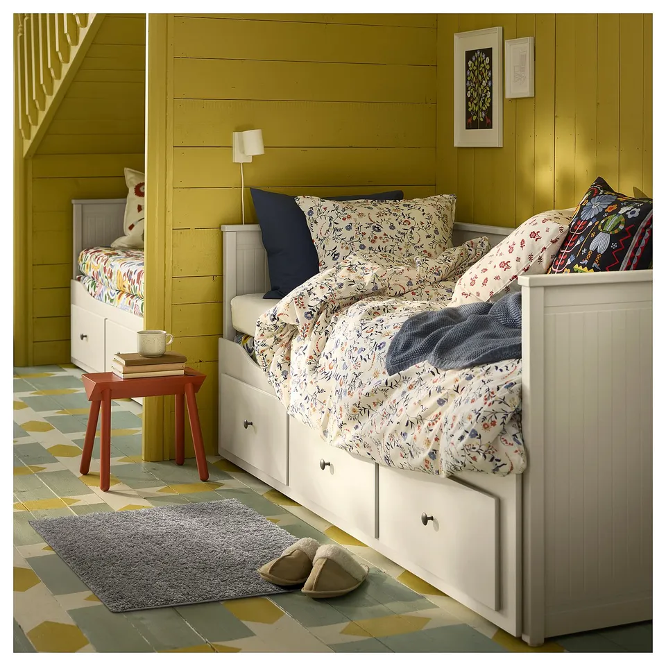 Cosy bedroom with white bed, floral bedding, red stool, grey rug, and yellow-green walls.