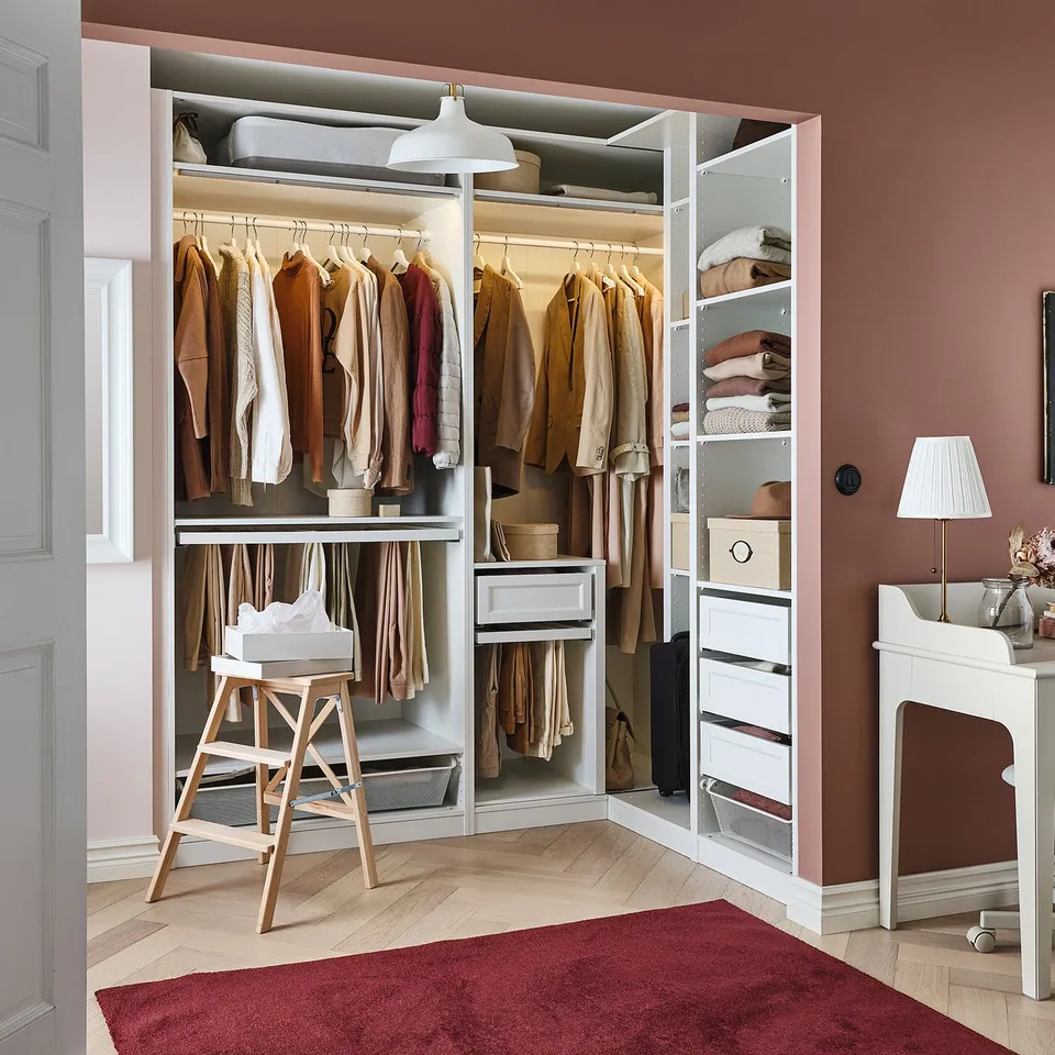 Neat walk-in closet with clothes, drawers, and organised shelves on pink walls.