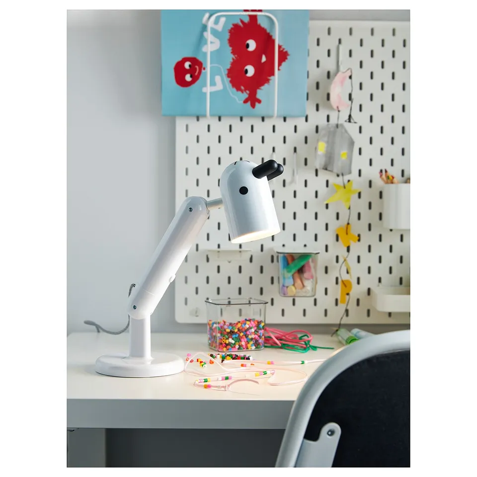 A childs craft desk with white KRUX lamp, colourful beads, star decoration, and fish poster on a pegboard wall.