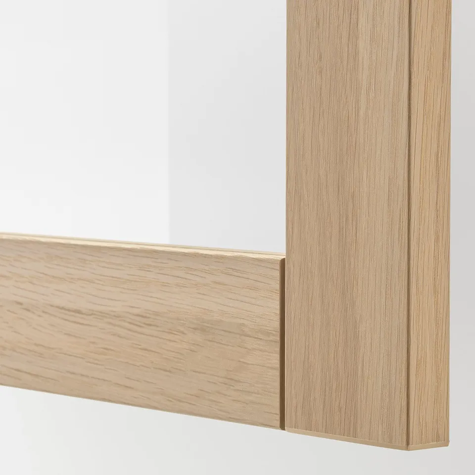A corner of a stylish, light wooden framed mirror. Smooth finish, sleek lines, modern design.