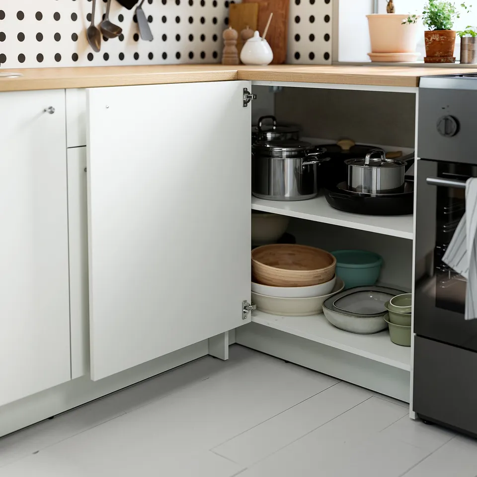 Open kitchen cabinet revealing organised pots, pans, bowls, and cutting boards neatly stored on its adjustable shelf.