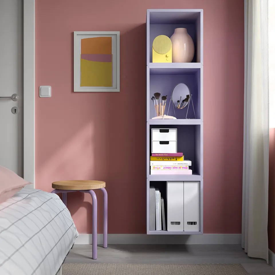 Wall-mounted purple EKET storage with shelves, holding books, makeup, decor, and a yellow stool. Space-saving.
