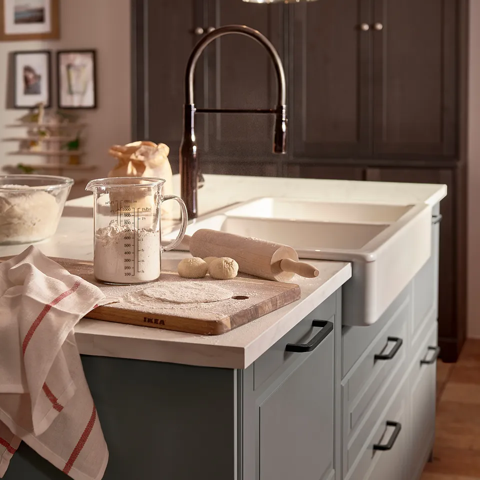 Modern kitchen sink with white & grey cabinets, black tap, wooden board, utensils, and red towel.