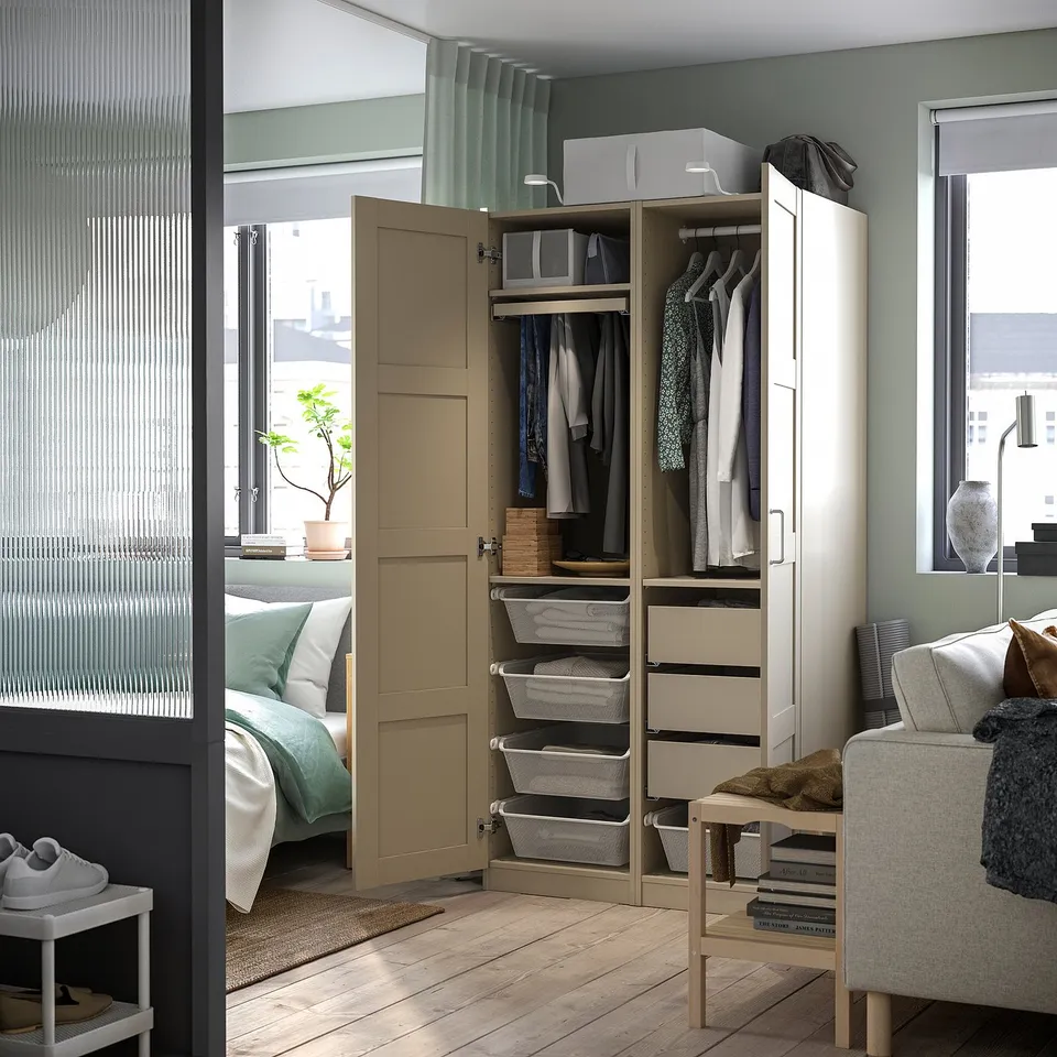 Modern bedroom with beige PAX wardrobe featuring clothes, drawers, and mesh baskets. Soft closing doors and grey curtains.