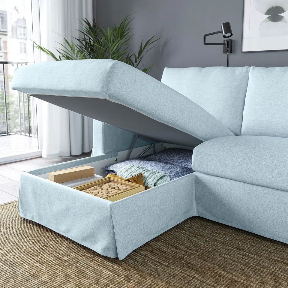 Light blue sofa with storage: lid open, revealing blankets and books inside the chaise. Modern home setting.