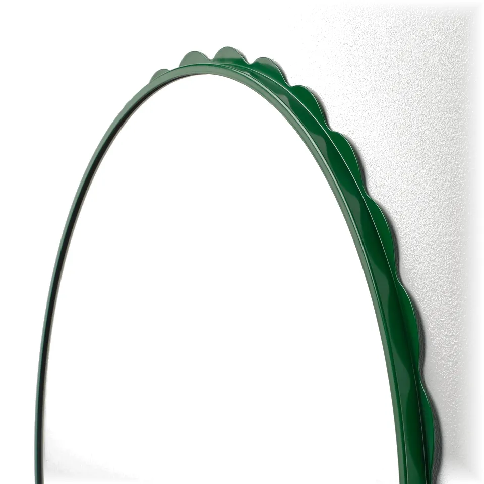 Green-framed mirror with a scalloped edge hangs on a wall. The glossy frame and clear reflection suggest high quality.