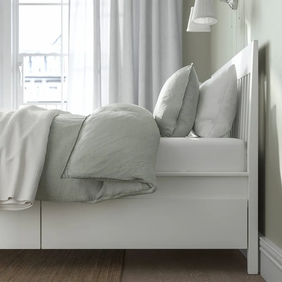 Cosy white bed with soft linens, two pillows, and built-in drawers for storage beneath, positioned near a large window.