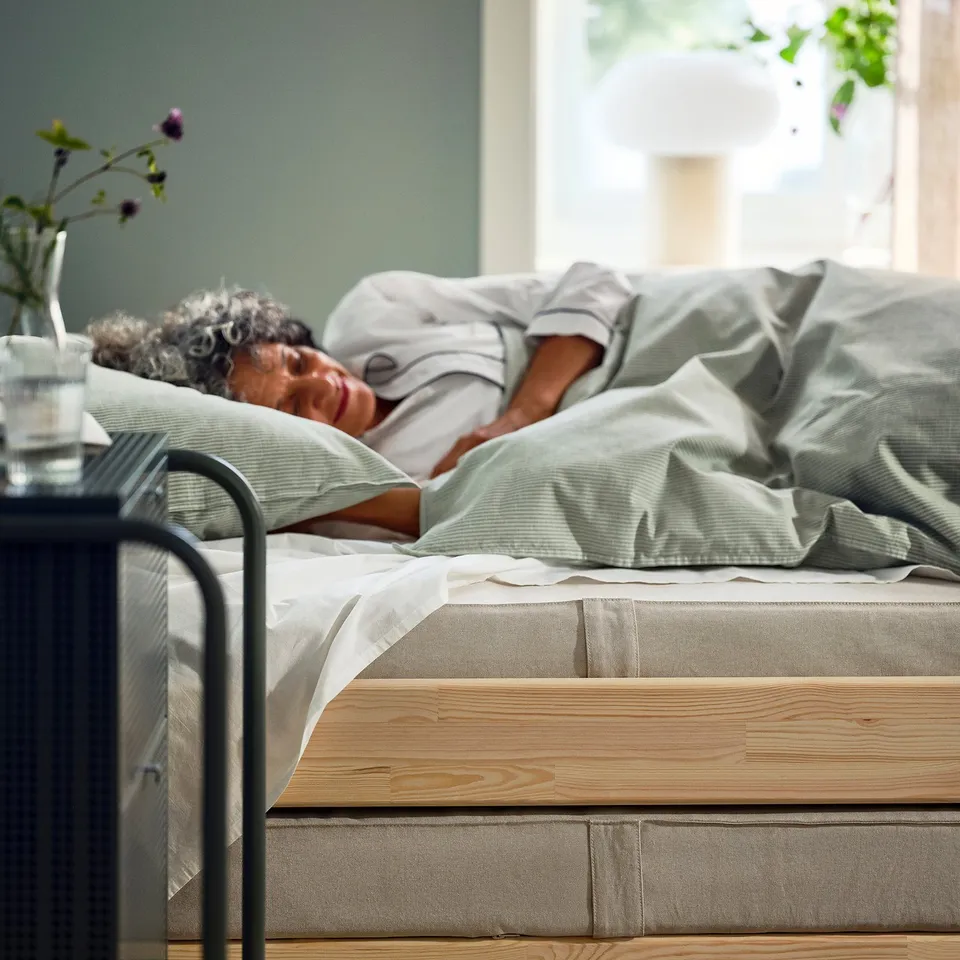 Person sleeps on VANNAREID mattress, grey, wooden frame.