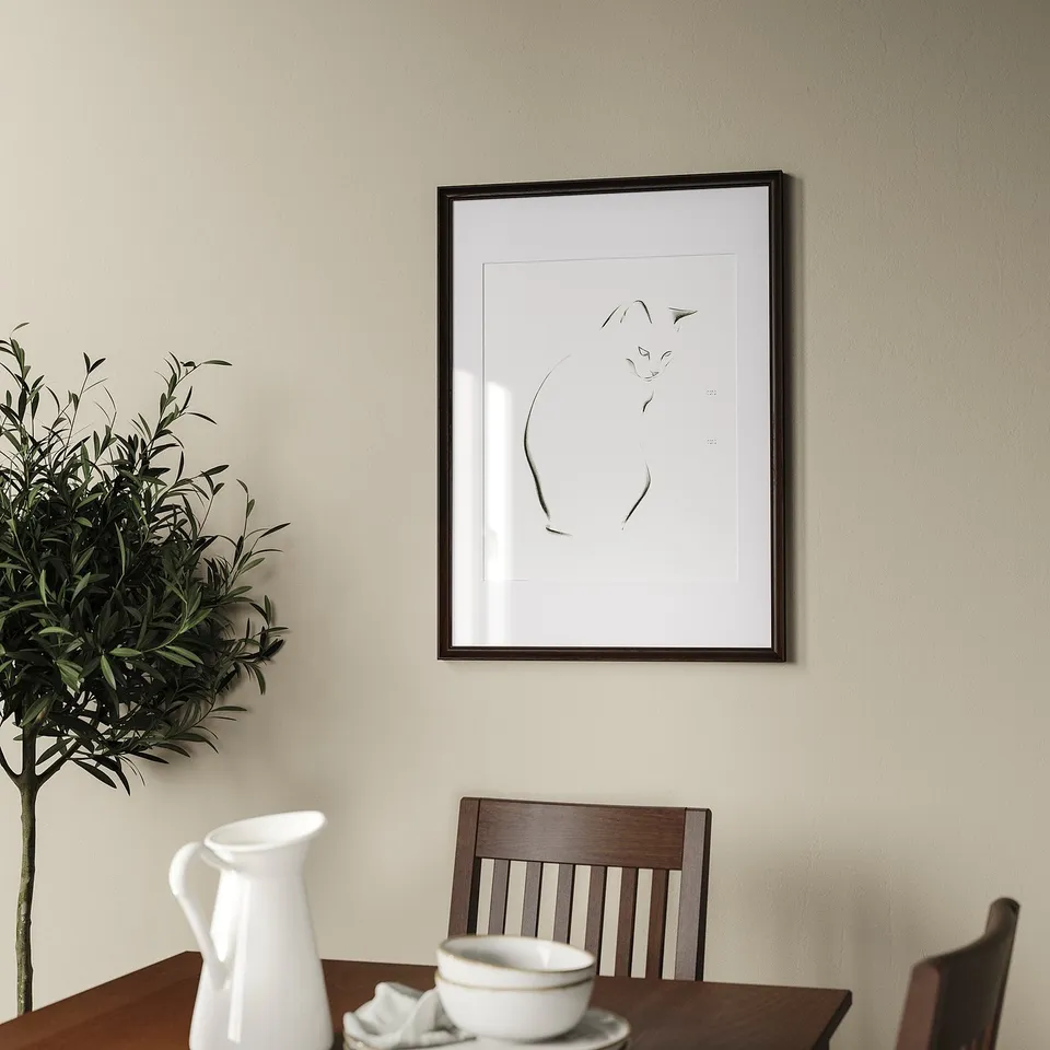 Framed picture hangs on wall above wooden table with chair. Plants in white vase, white pitcher, and bowl shown on table.