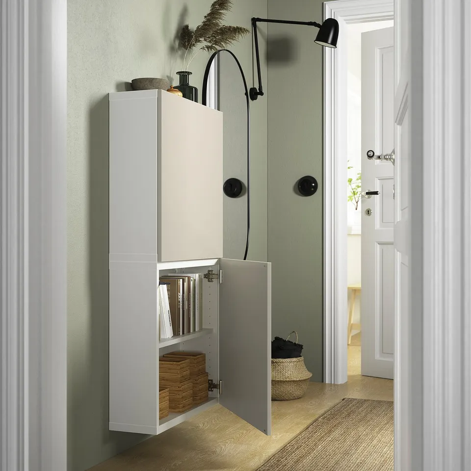 White BESTÅ cabinet, wall-mounted, with one door open revealing inner shelves and baskets. Light wood floor, green wall, adjustable shelf inside.