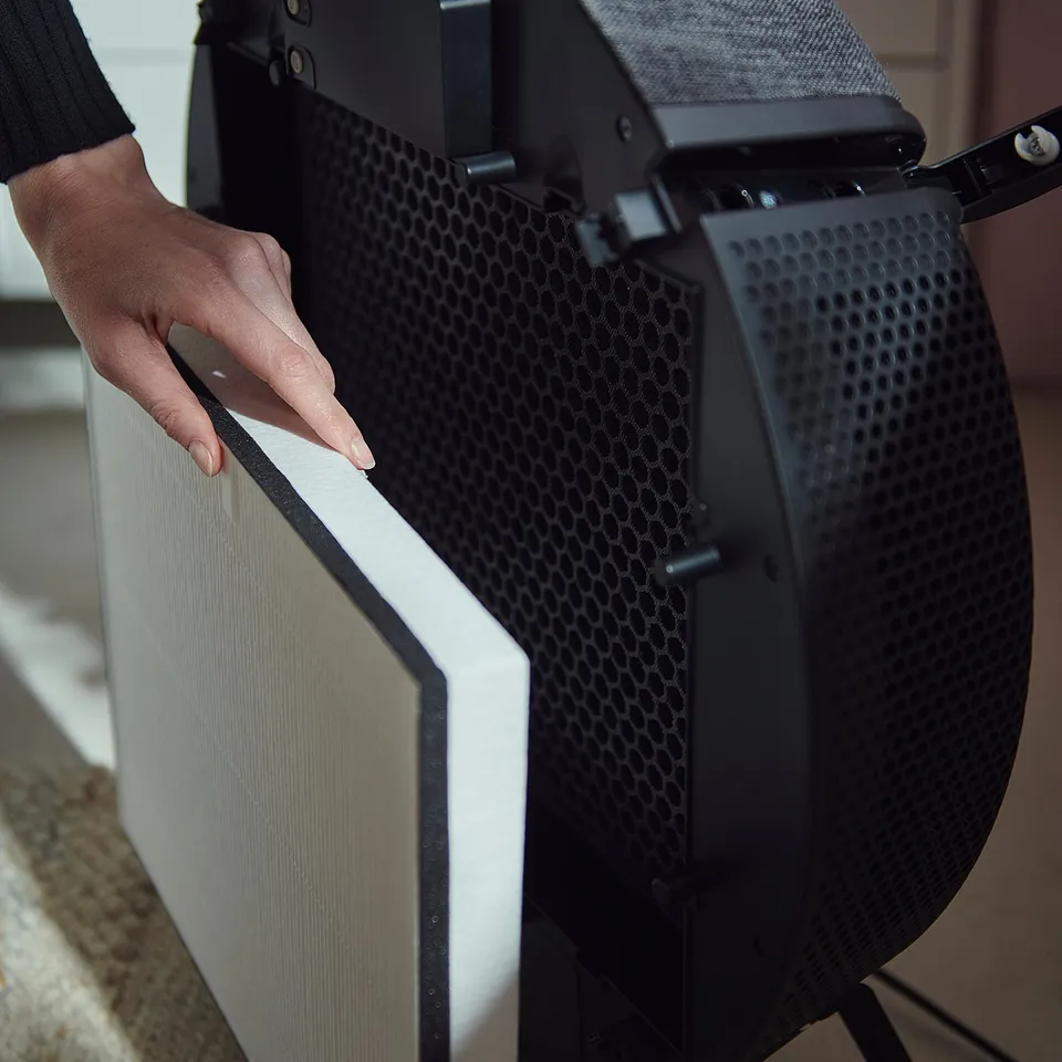 A person handles a black STARKVIND air purifier. Its front has honeycomb holes and a removable philtre.