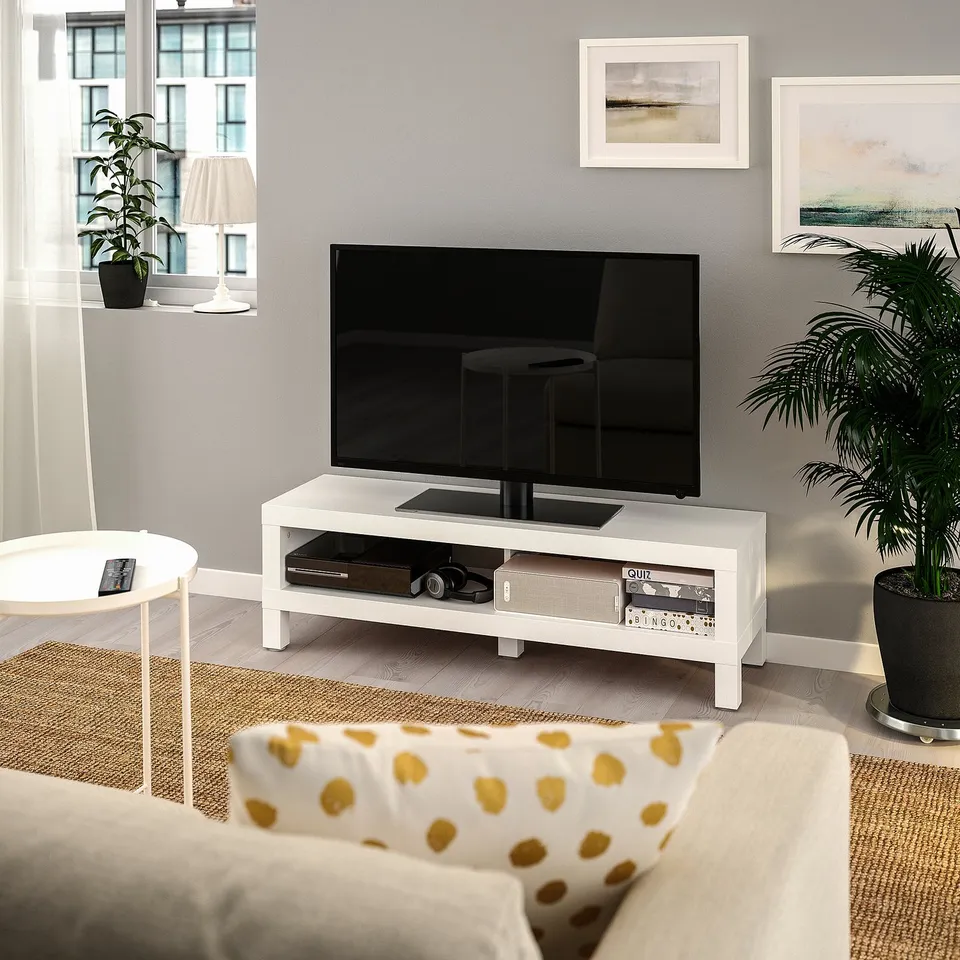 Modern living room with LACK tv stand, flat-screen, and yellow dotted couch. Windows, side table with lamp, and abstract paintings on grey walls.