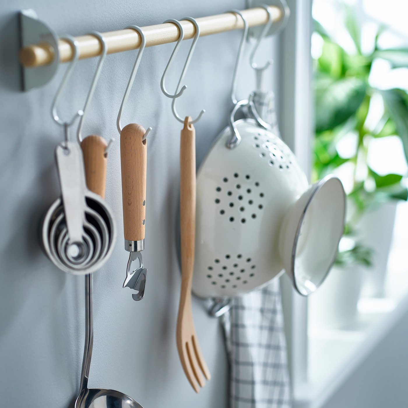 Kitchen tools hang neatly on wall hooks. Includes measuring cups, can opener, strainer, and spatula, all with wooden handles, ready for use.