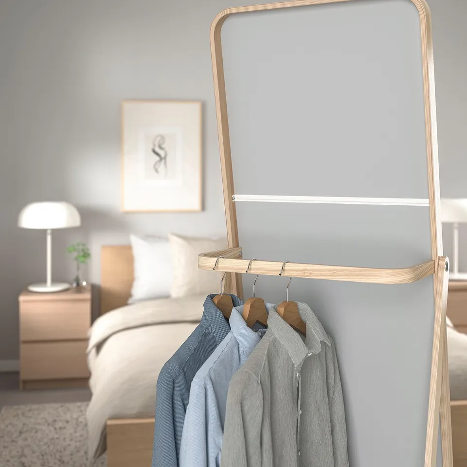 Light wooden clothes rack with mirror hangs shirts beside bed for easy morning access.