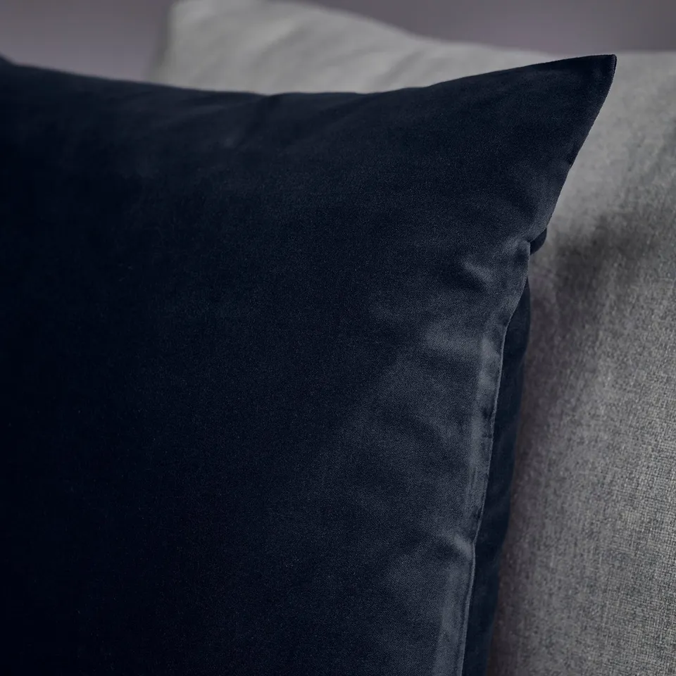 Dark blue velvet cushion cover on a grey surface, showcasing its soft, luxurious texture.