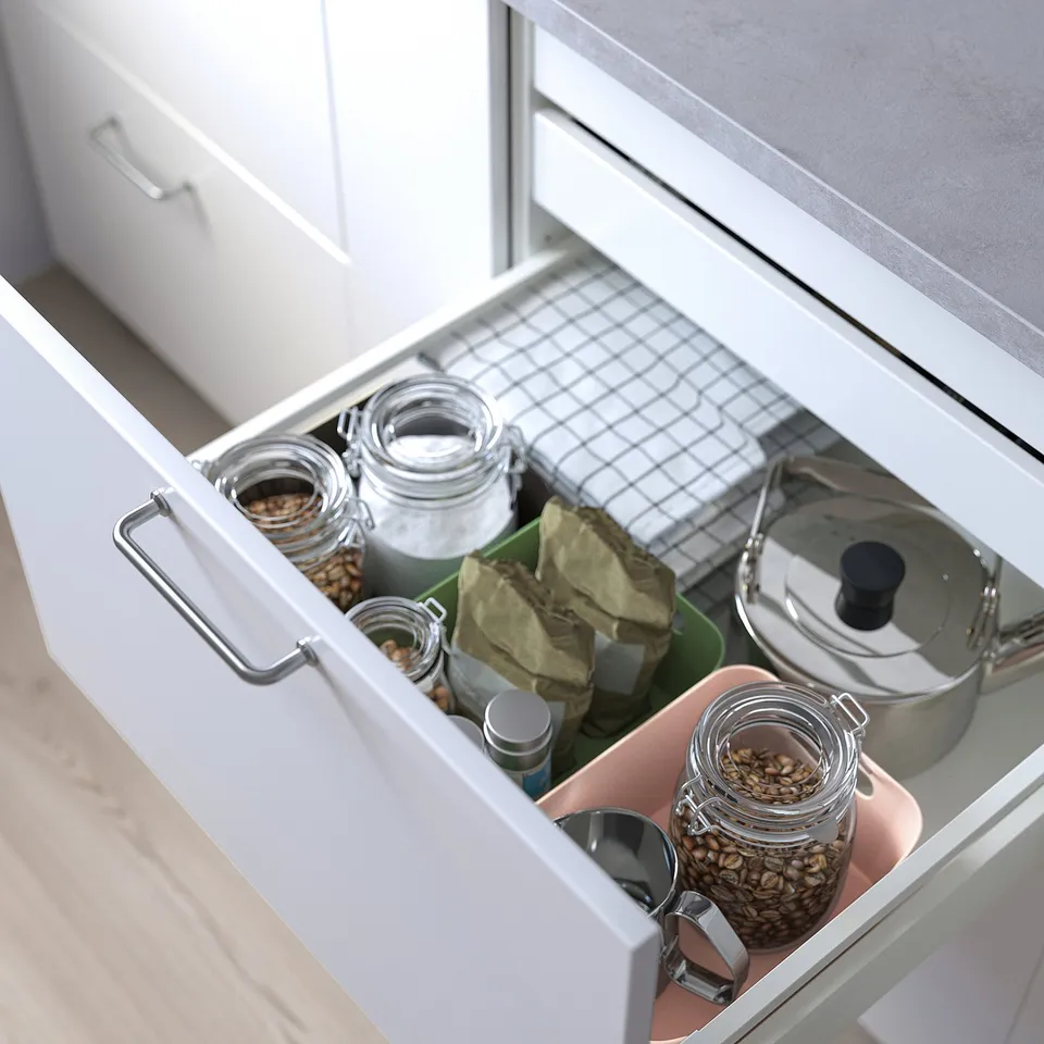 Open kitchen drawer revealing organiser boxes with glass jars storing seeds and nuts, and a metal lid on a cloth.