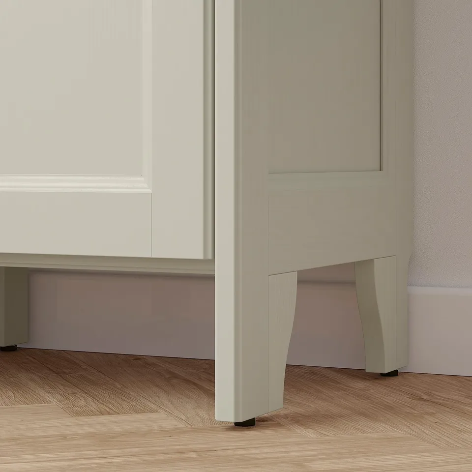 A modern storage units leg and panel shown. Off-white, sturdy, wooden design with cut-outs, on a wooden floor.