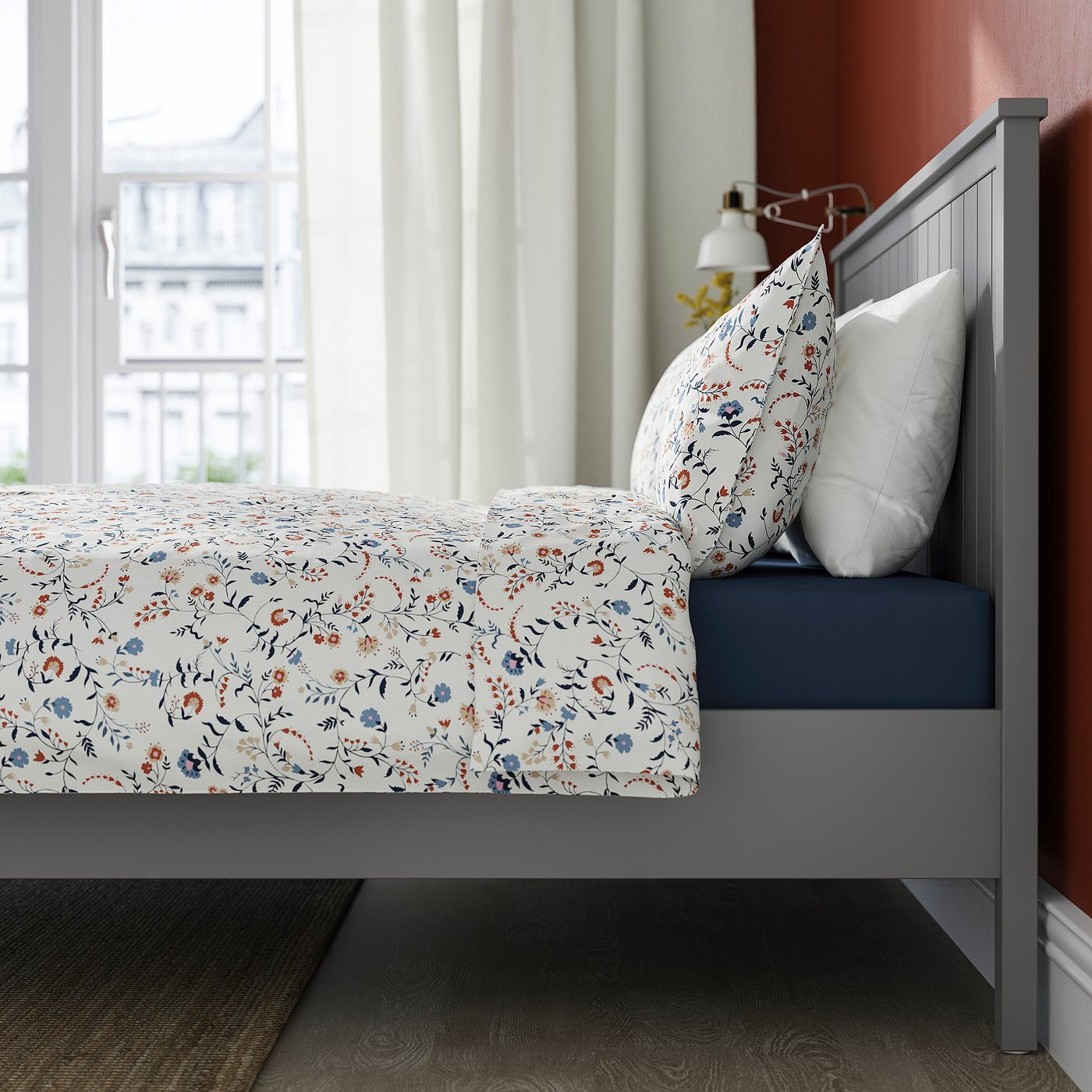 A grey GULLABERG bed with a floral bedspread and white pillows. The bed has a centre support beam.