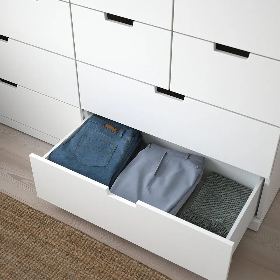 Open white NORDLI drawer showing neatly folded blue jeans and grey pants. Part of wider chest unit.