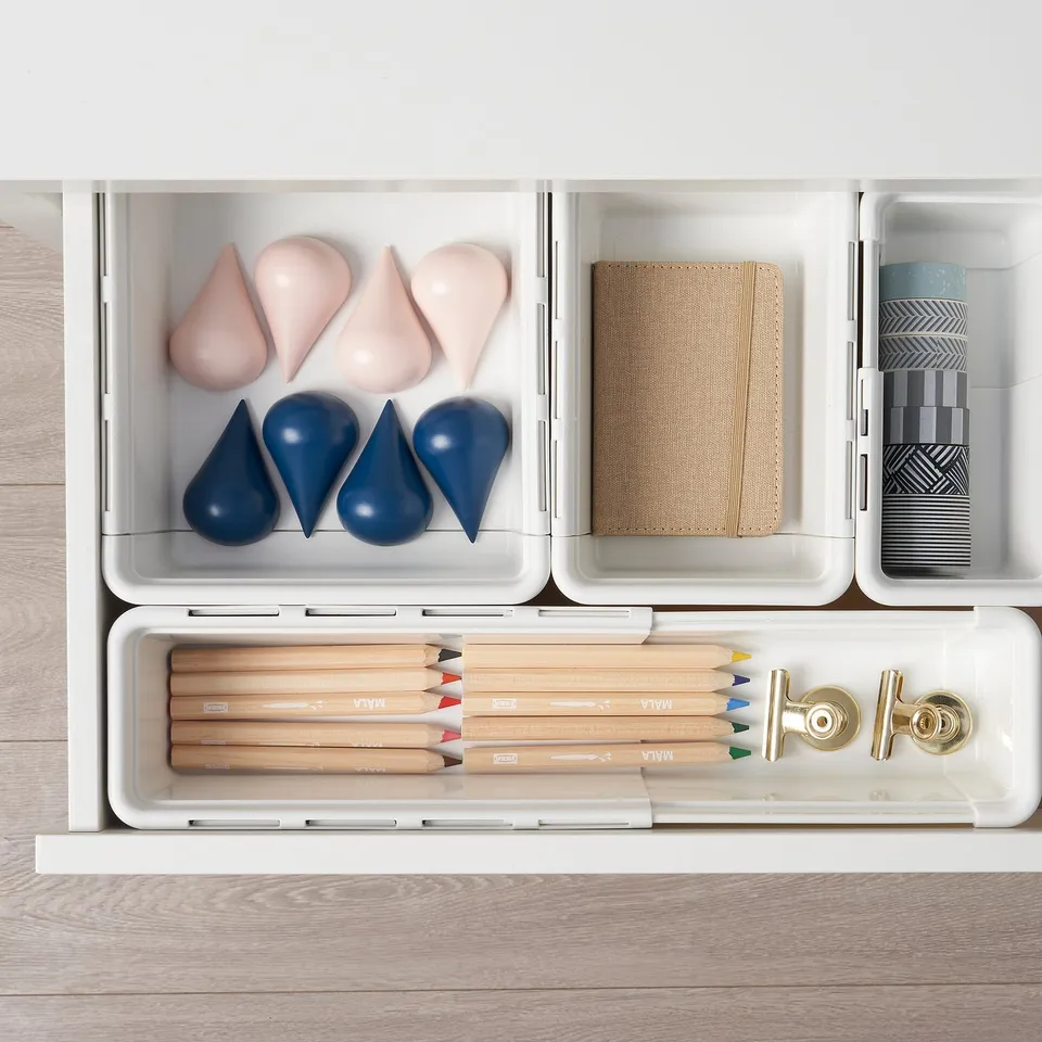 Open drawer with art supplies: coloured pencils, elastics, and fabric samples in organised containers.