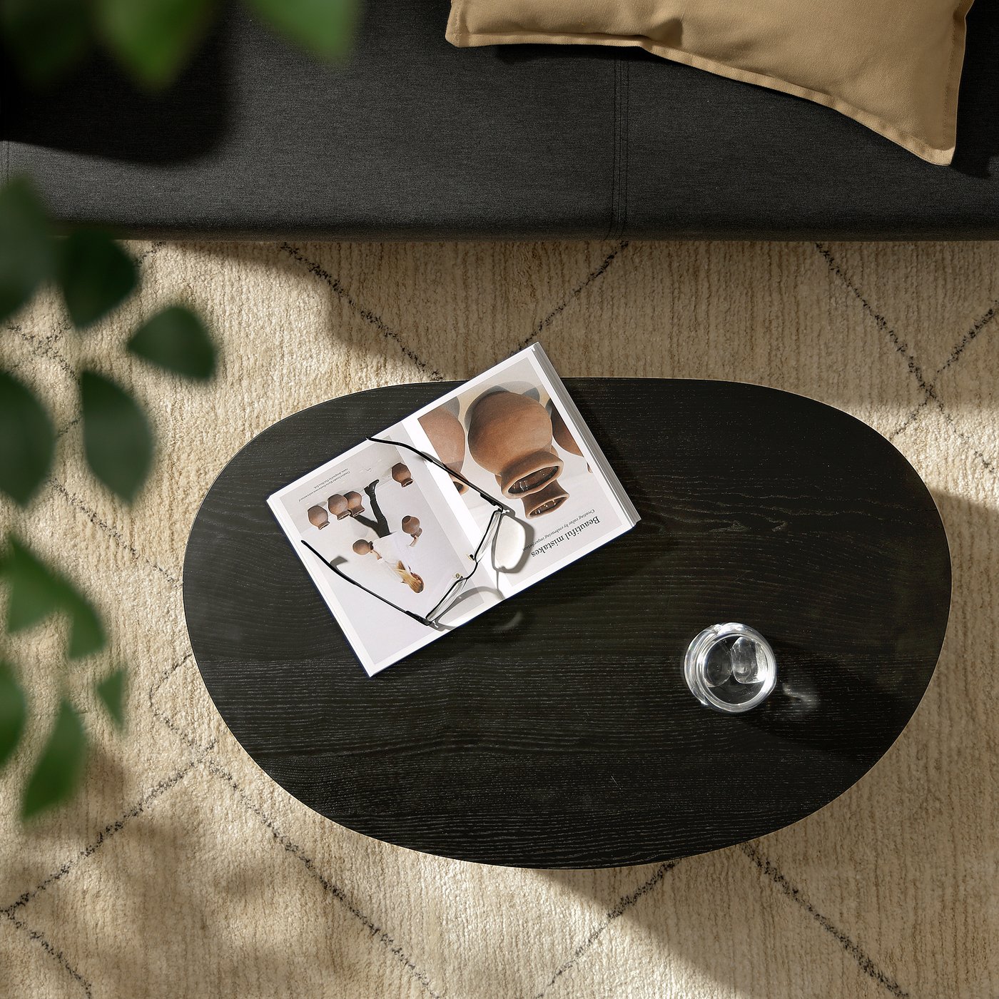Dark wood round coffee table with magazine, glasses, on beige shaggy rug beside black sofa.