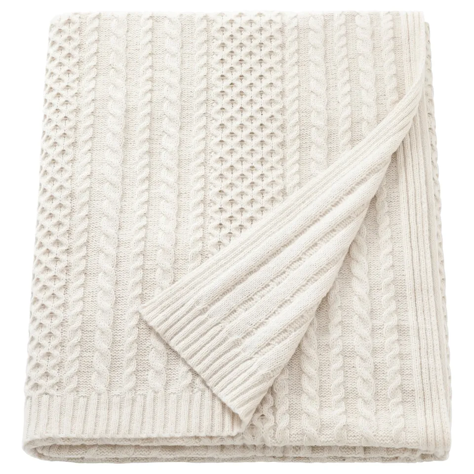 A white SÖRBYSKOGEN blanket made of 100% recycled polyester. It a folded cable knit design.