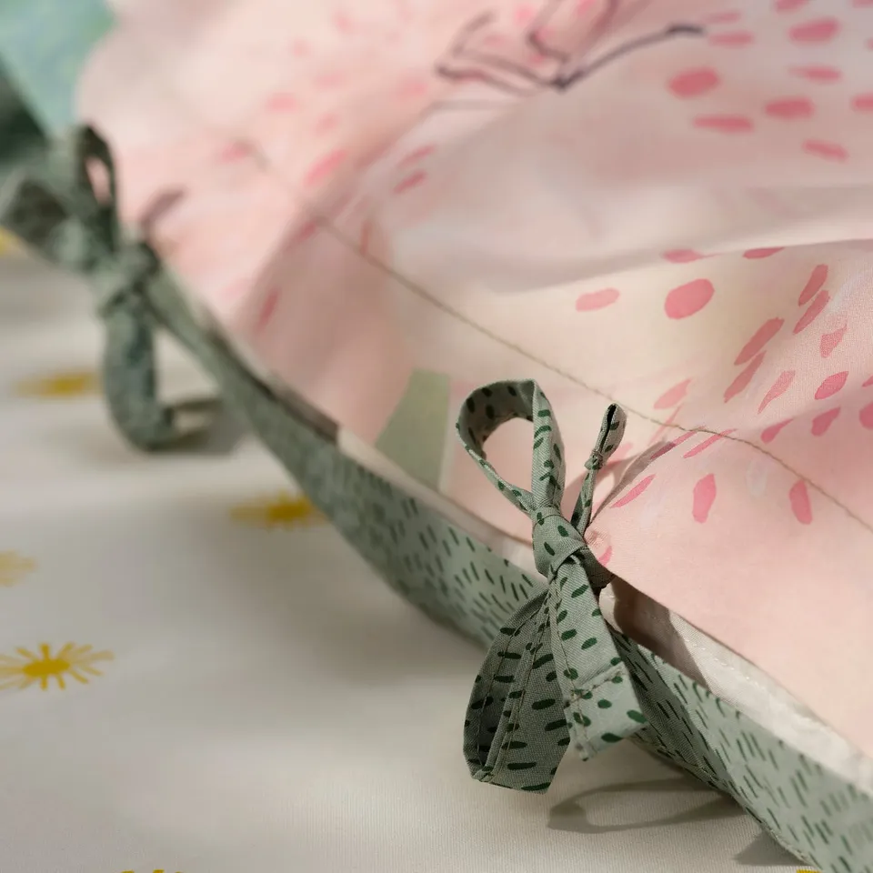 A close-up of a pink duvet cover with green dot ribbon ties, showcasing its double-sided nature.