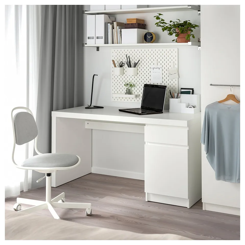 Clean, minimalist home office a white MALM desk with a matching chair, laptop, and pegboard storage.