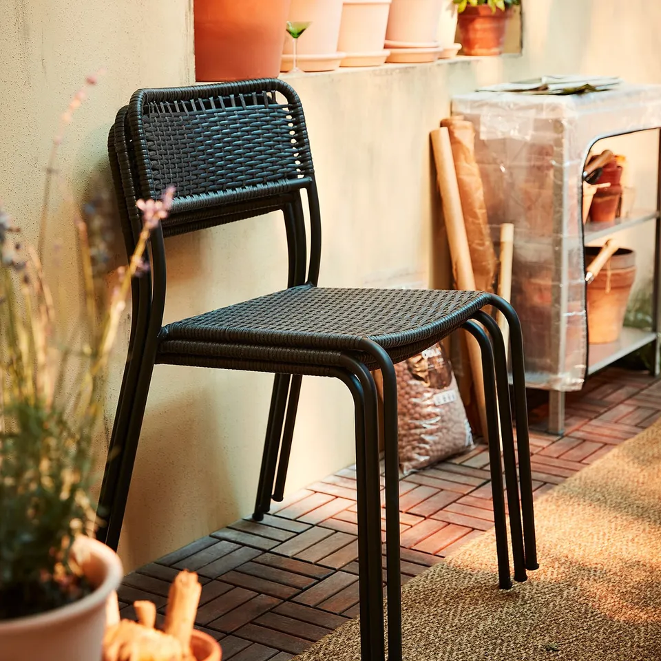 Black wicker chair on tiled patio, surrounded by potted plants, creating a cosy garden seating area.