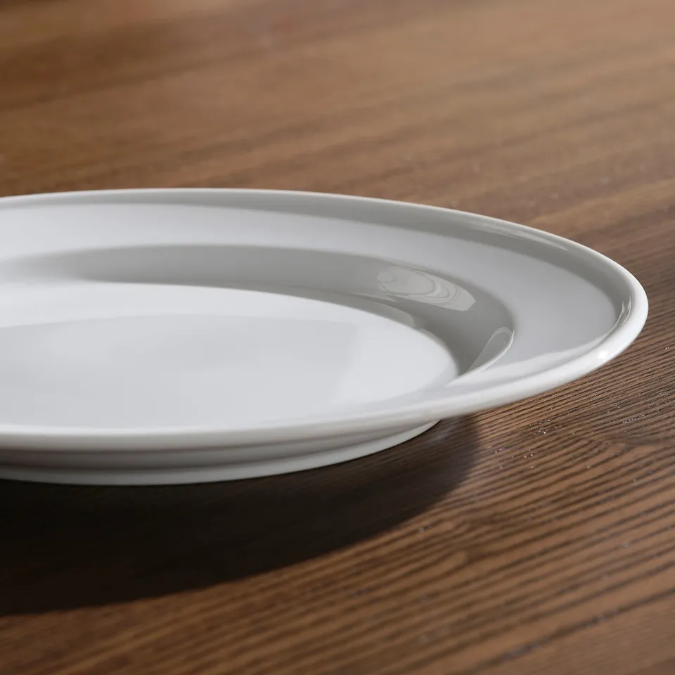 Two white porcelain plates stacked on a wooden table, showcasing their smooth, elegant rims and durable quality.
