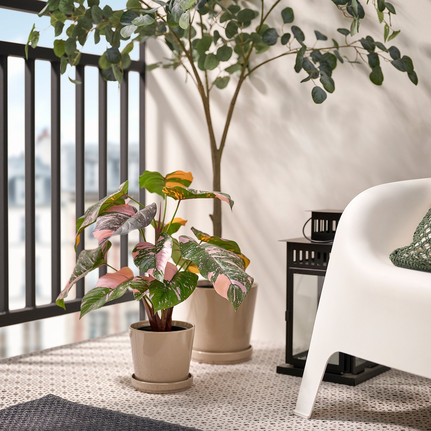 Small FEJKA potted plant sits beside a white chair on a balcony, with metal railings and a larger plant nearby.