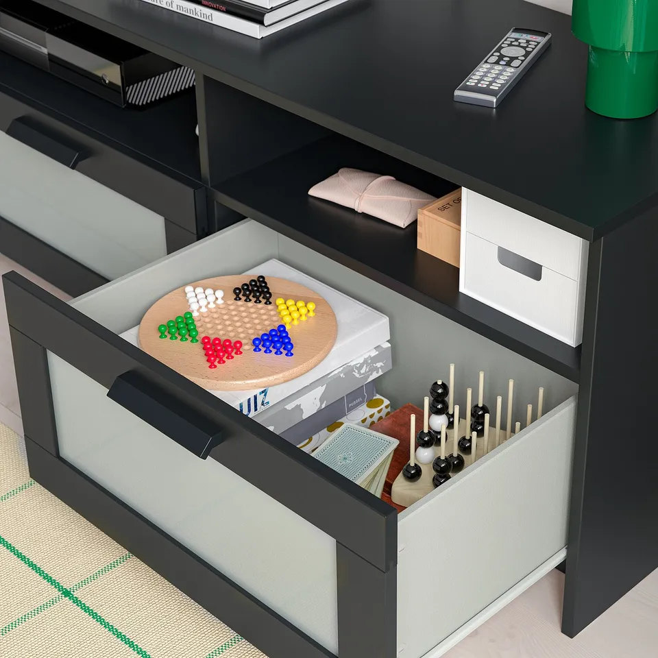 Tv stand with open drawer showcasing games and accessories, including a board game with coloured pieces and remote controls.