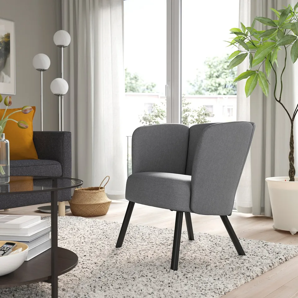 Modern living room with grey upholstered HERRÅKRA chair, sleek design, near large window, cosy rug, and potted plant.
