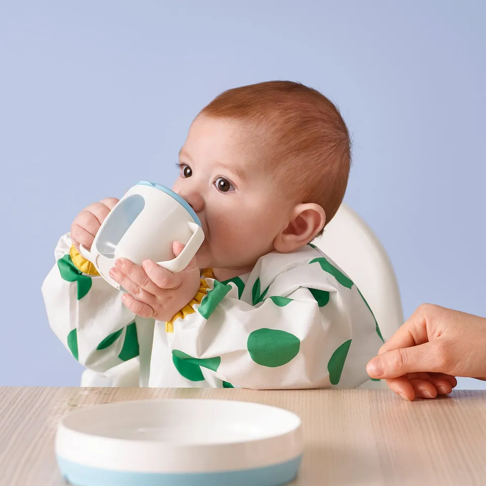 Baby drinks from two-handled beaker with spout