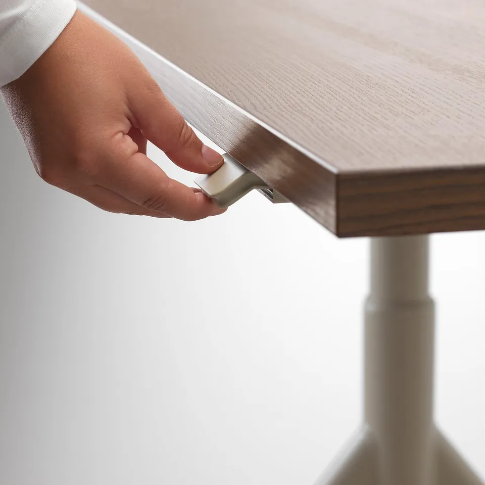 A hand adjusts an IDÅSEN desk, showing height control feature.