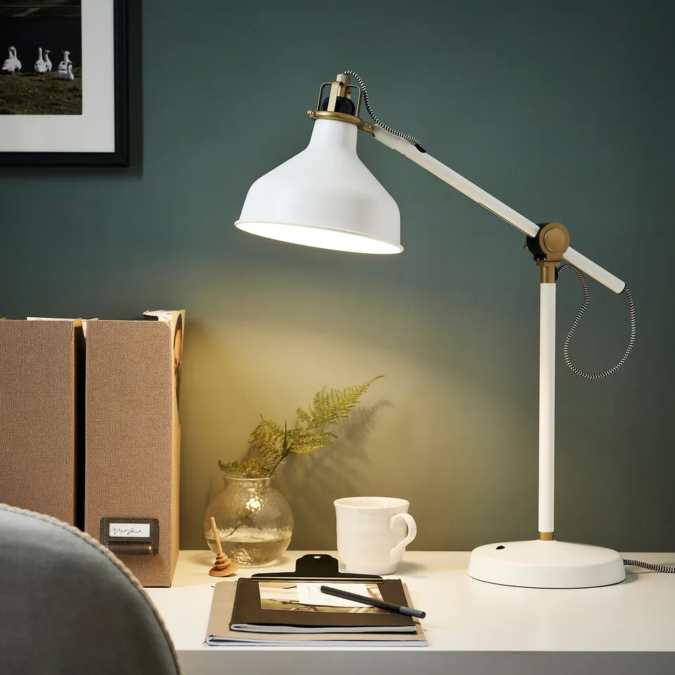 RANARP lamp illuminates workspace with notebook, mug, and plant.